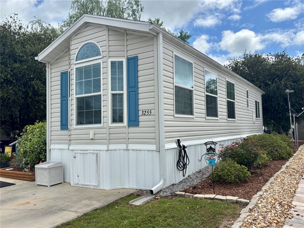 A beige mobile home with blue shutters and a white skirt sits on a lot — 3255 NE 104TH AVENUE, SILVER SPRINGS, FL