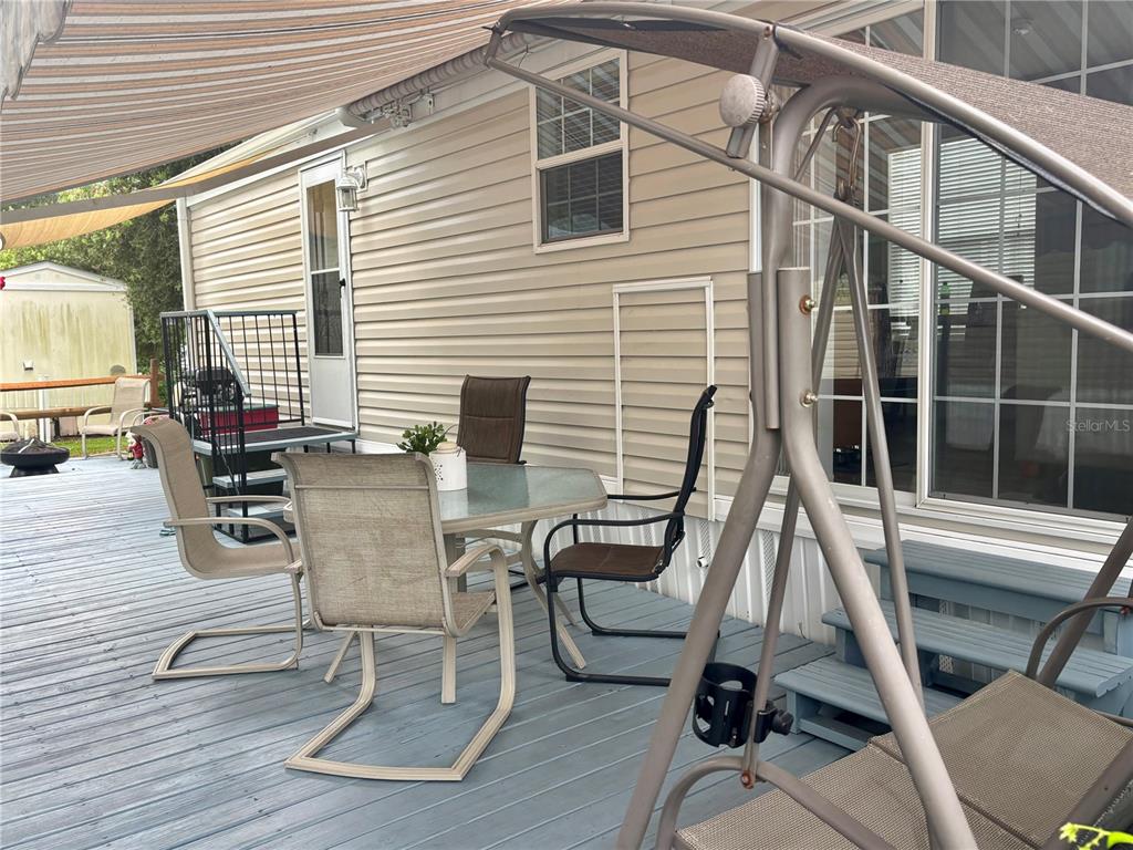 A wooden deck features patio furniture, a swing, and a retractable awning beside a house — 3255 NE 104TH AVENUE, SILVER SPRINGS, FL