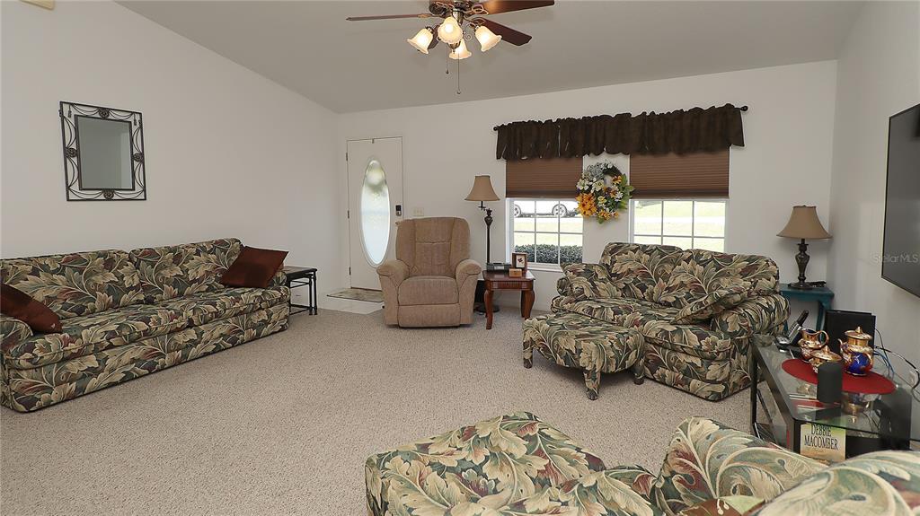 A carpeted living room features floral patterned furniture, a ceiling fan, and a front door — 13777 SE 44TH AVENUE, SUMMERFIELD, FL