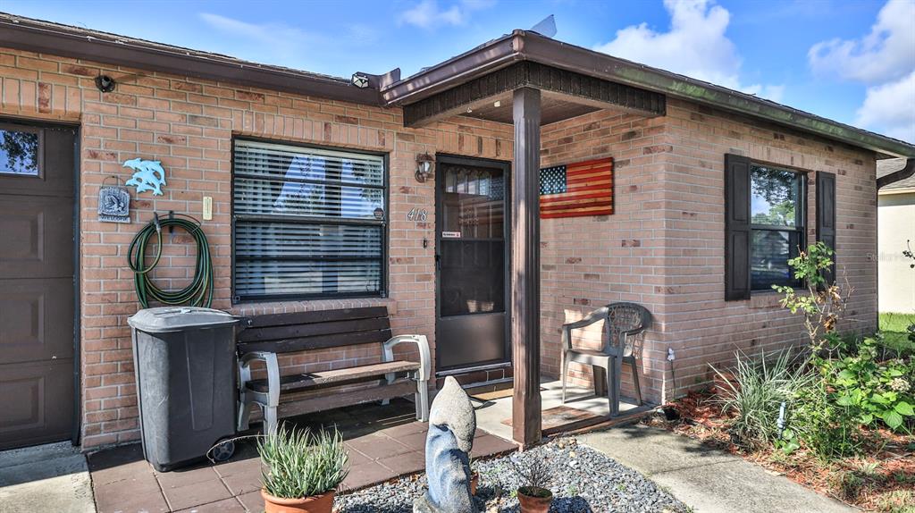 A brick house exterior features a front porch, a wooden bench, and an American flag — 418 FALCON AVENUE, EDGEWATER, FL