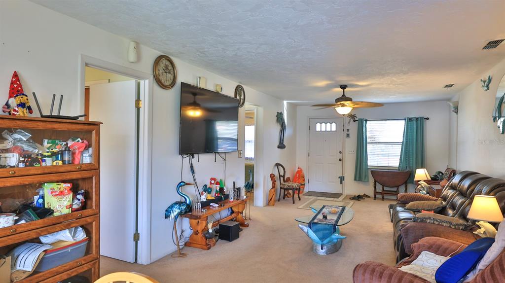 A living room features a wall-mounted television, a ceiling fan, and a brown leather sofa — 418 FALCON AVENUE, EDGEWATER, FL