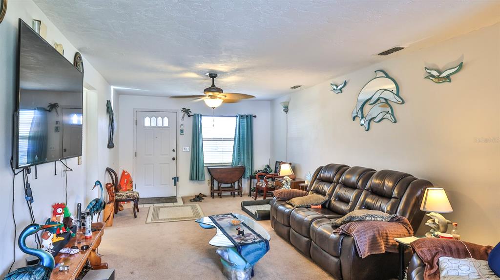 A living room features a brown leather sofa, a glass coffee table, and dolphin wall decor — 418 FALCON AVENUE, EDGEWATER, FL