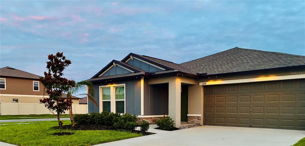 A single-story house with a blue exterior, a two-car garage, and a manicured front lawn — 2141 LANIER ROAD, ZEPHYRHILLS, FL