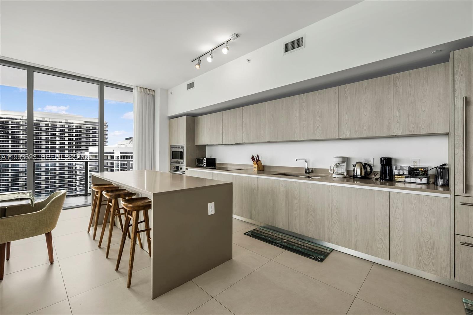A modern kitchen features light wood cabinetry, a large island with bar stools, and floor-to-ceiling windows — 4111 S Ocean Dr, Hollywood FL 33019, HOLLYWOOD, FL