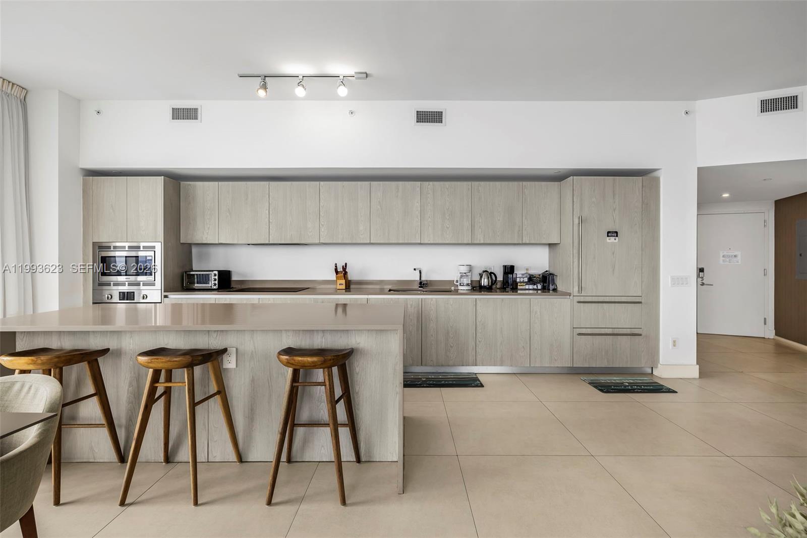 A modern kitchen features light wood cabinetry, a large island with bar stools, and tile flooring — 4111 S Ocean Dr, Hollywood FL 33019, HOLLYWOOD, FL