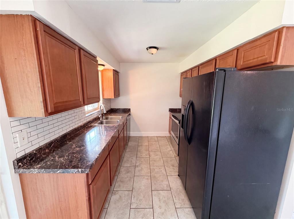 A galley kitchen features wood cabinets, dark laminate countertops, a black refrigerator, and tile flooring — 7026 HAMMOCK WAY, WINTER PARK, FL