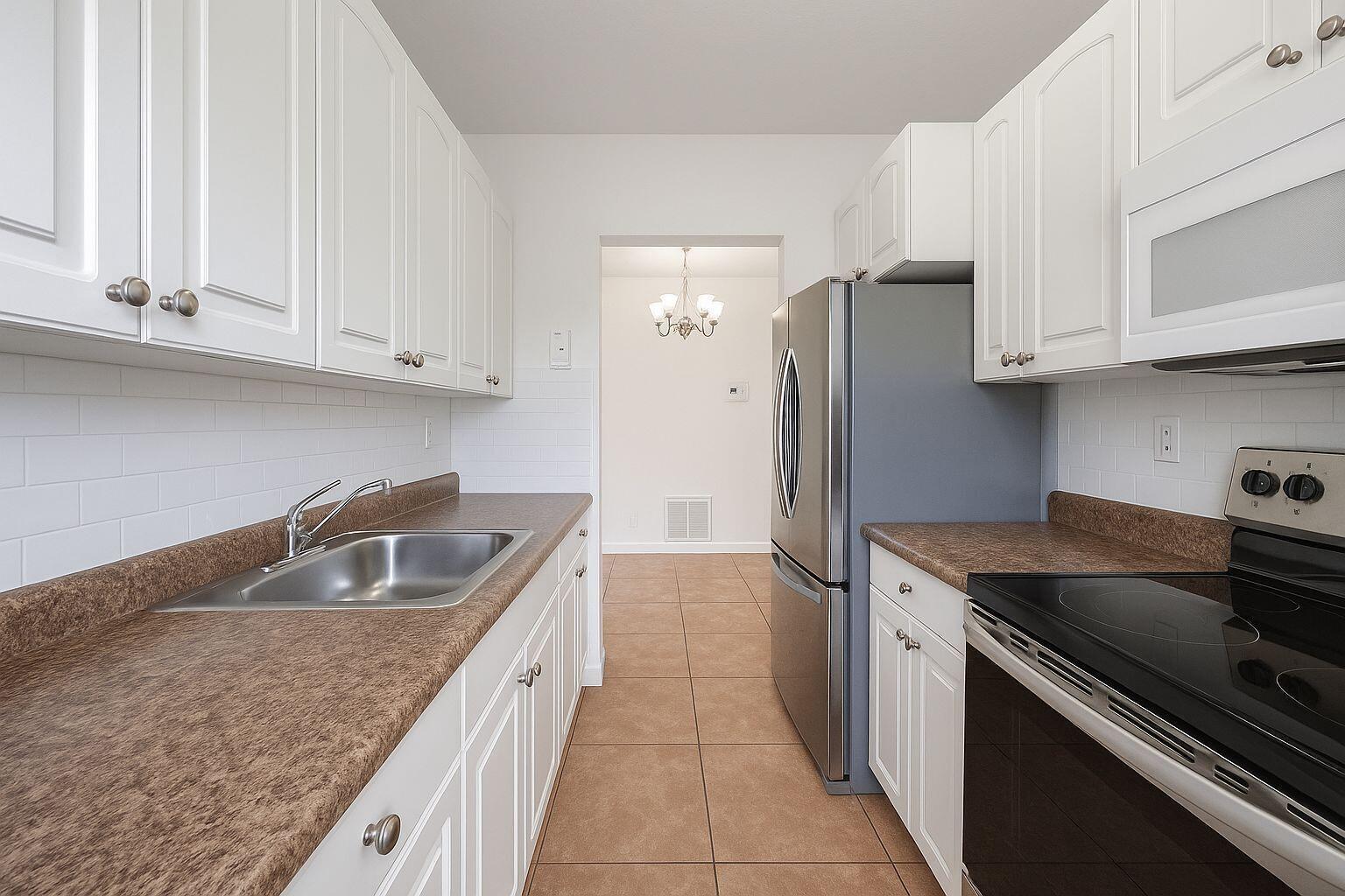 A galley kitchen features white cabinets, brown countertops, stainless steel appliances, and tile flooring — 3390 NE 16th Terrace # 5, Pompano Beach FL 33064, POMPANO BEACH, FL