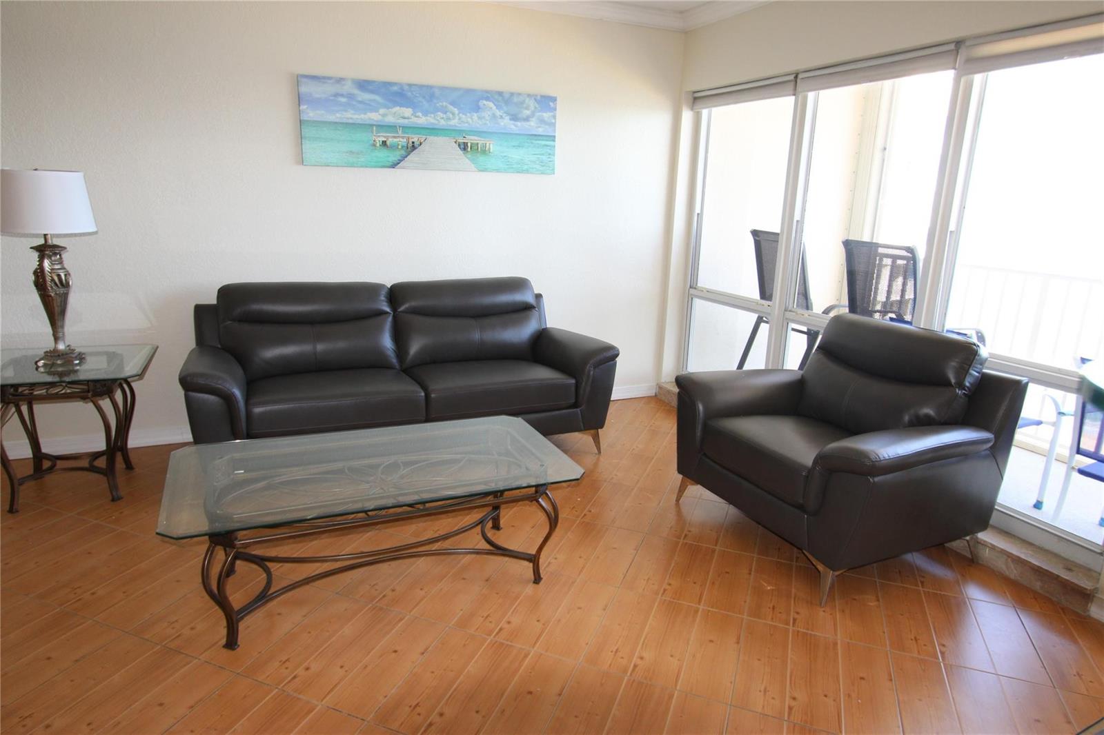 A living room features dark leather furniture, a glass coffee table, and tile flooring — 750 N Ocean Boulevard # 1709, Pompano Beach FL 33062, POMPANO BEACH, FL
