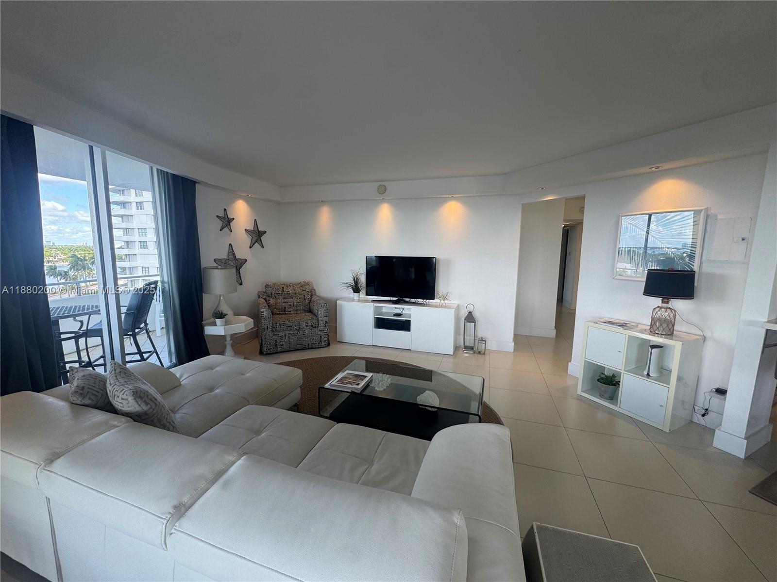 A living room features a white sectional sofa, a glass coffee table, and a balcony — 5151 Collins Ave # 923, Miami Beach FL 33140, MIAMI BEACH, FL