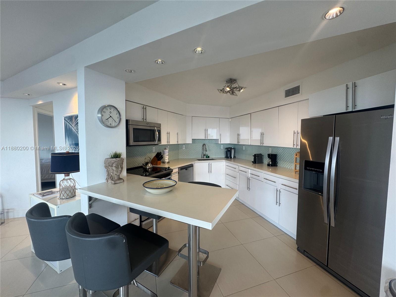 A modern kitchen features white cabinetry, stainless steel appliances, and a breakfast bar with stools — 5151 Collins Ave # 923, Miami Beach FL 33140, MIAMI BEACH, FL