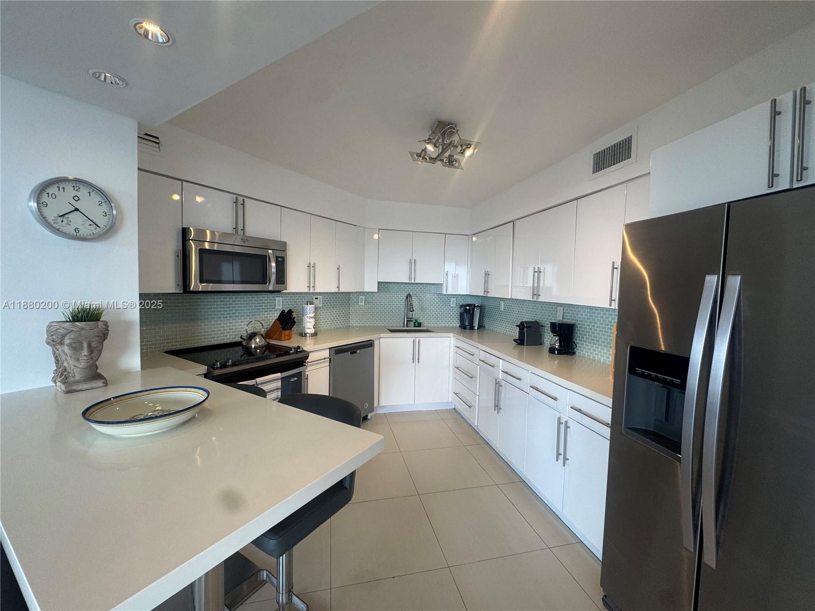 A modern kitchen features white cabinets, stainless steel appliances, and a light blue tiled backsplash — 5151 Collins Ave # 923, Miami Beach FL 33140, MIAMI BEACH, FL