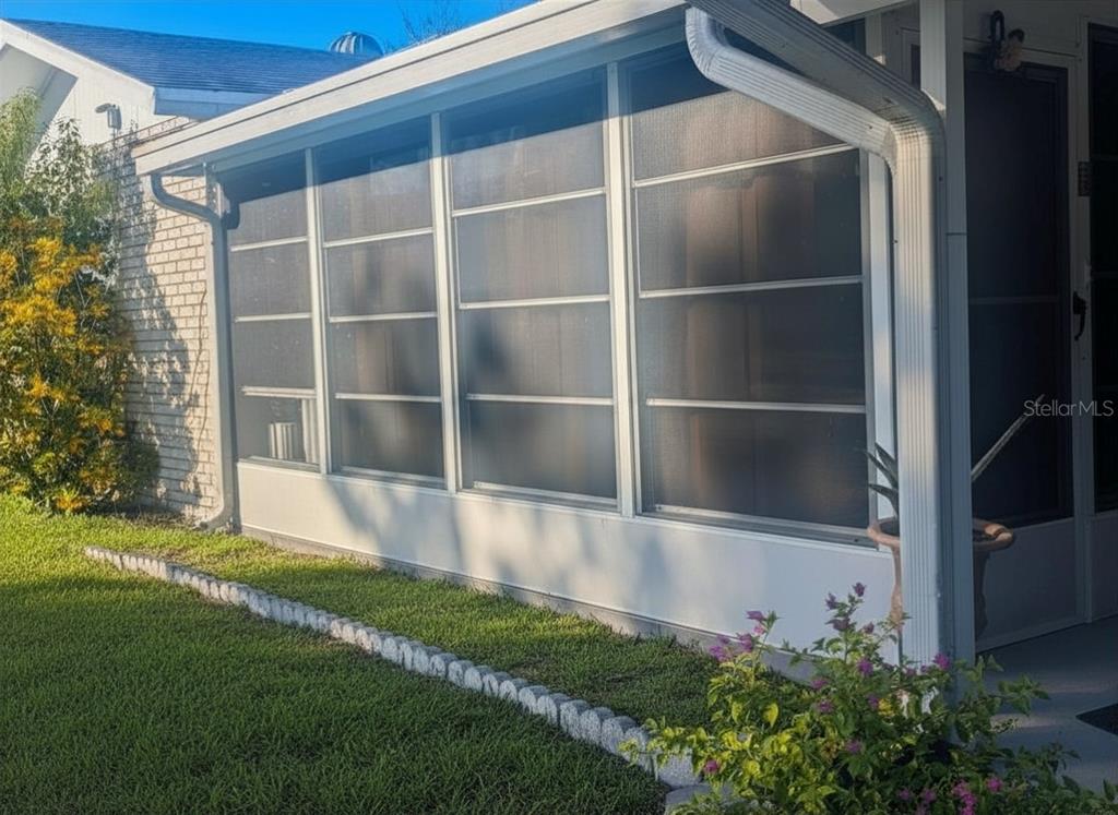 A white-framed screened-in porch with horizontal sliding windows sits beside a brick exterior wall — 3602 CONNOR AVENUE, ORLANDO, FL