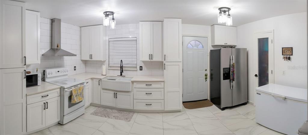 A bright kitchen features white cabinets, stainless steel appliances, a farmhouse sink, and tile flooring — 3602 CONNOR AVENUE, ORLANDO, FL