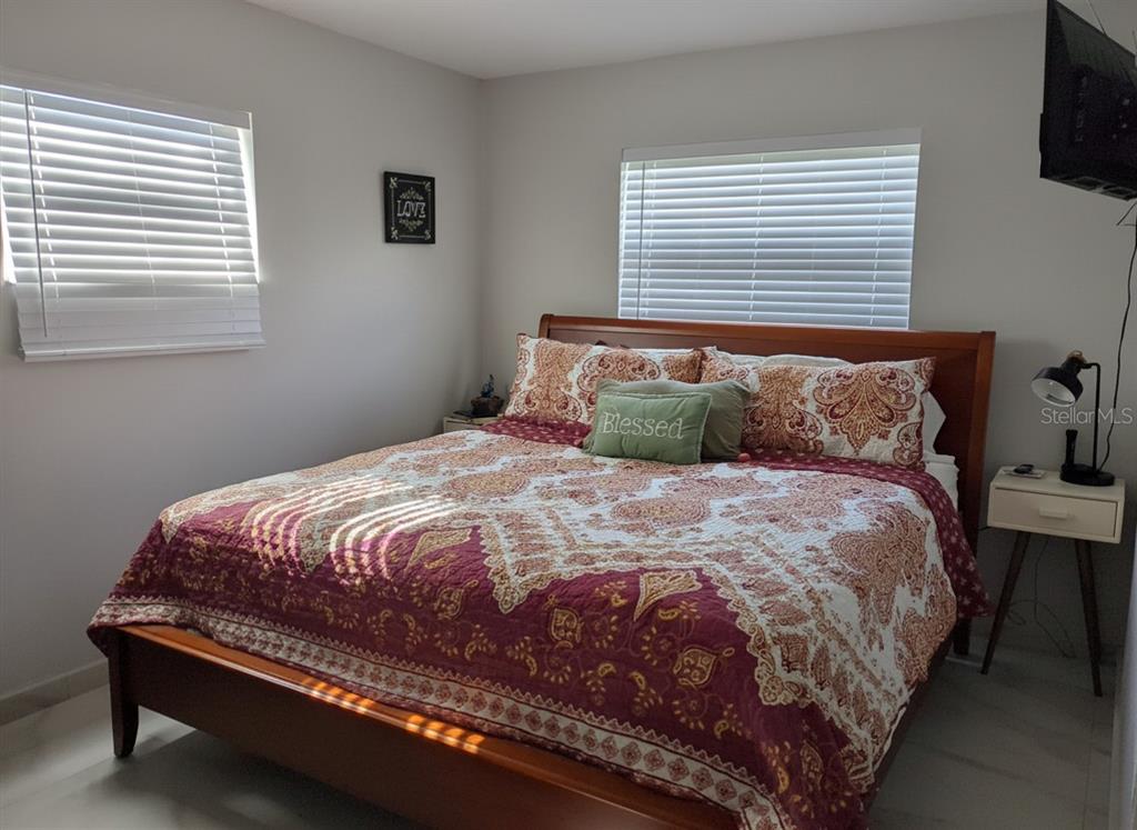 A bedroom features a wooden bed frame, patterned bedding, two windows with blinds, and a nightstand — 3602 CONNOR AVENUE, ORLANDO, FL