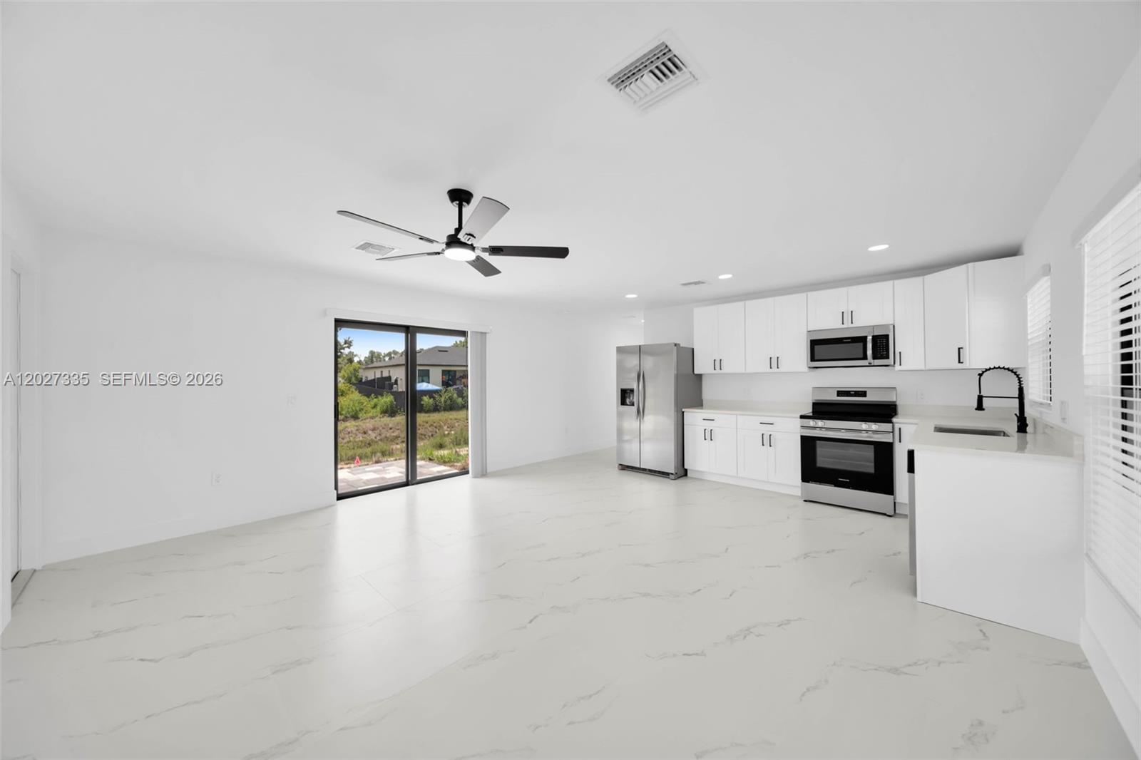 A bright, open-concept kitchen and living area features white cabinetry, stainless steel appliances, and flooring — 4985 Fairway Ct # 4985, Lehigh Acres FL 33971, LEHIGH ACRES, FL
