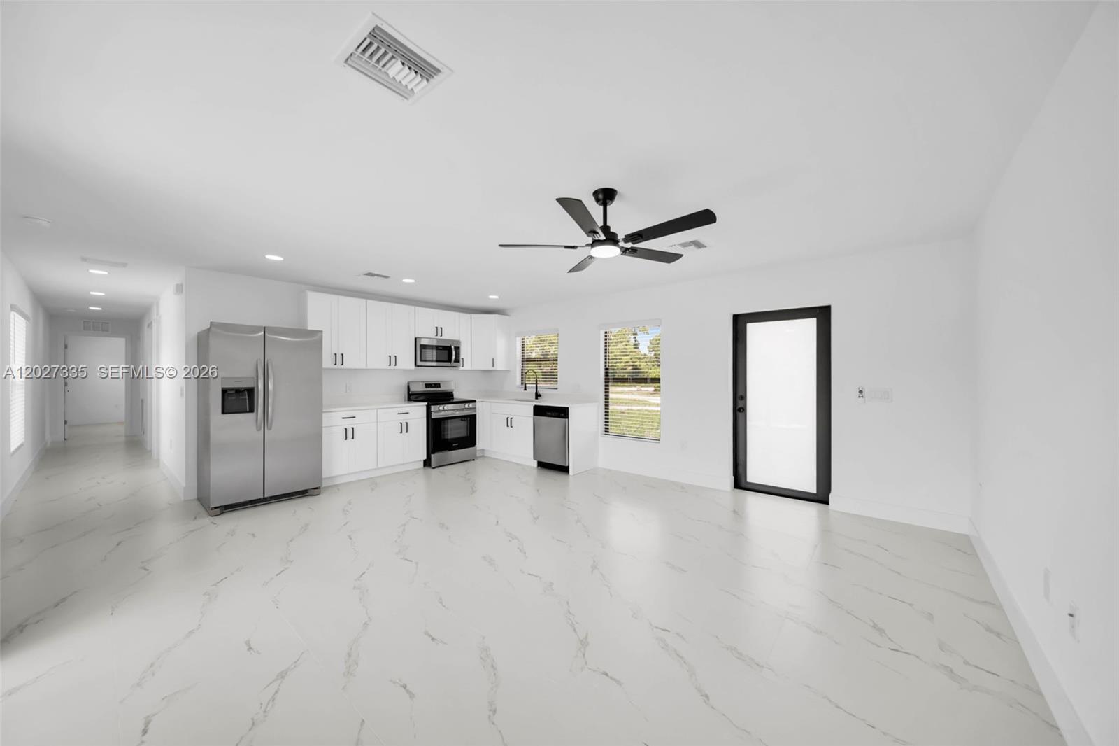 A modern kitchen features white cabinets, stainless steel appliances, and white marble-patterned tile flooring — 4985 Fairway Ct # 4985, Lehigh Acres FL 33971, LEHIGH ACRES, FL