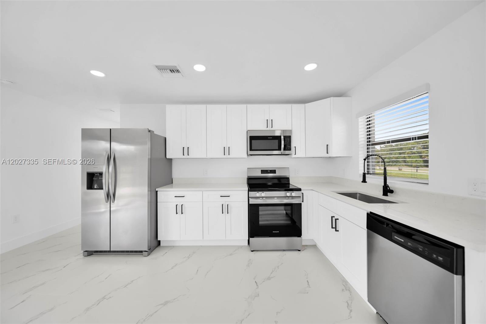 A modern kitchen features white cabinets, stainless steel appliances, and white marble-patterned tile flooring — 4985 Fairway Ct # 4985, Lehigh Acres FL 33971, LEHIGH ACRES, FL