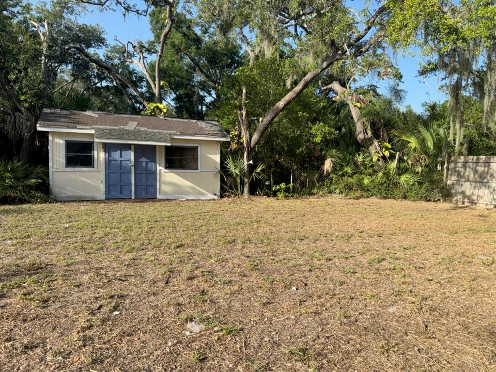 A small, light-colored shed with blue double doors sits in a grassy backyard — 9901 DAVIS STREET, GIBSONTON, FL