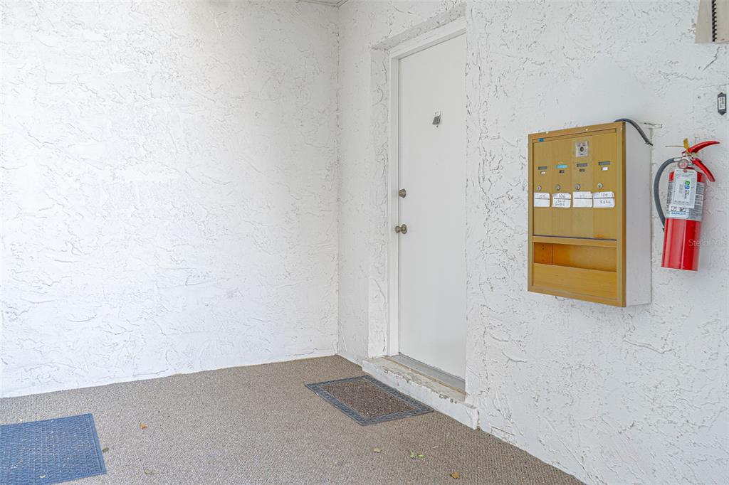 A white door is flanked by a wall-mounted mailbox unit and a red fire extinguisher — 363 S MCMULLEN BOOTH ROAD UNIT 107, CLEARWATER, FL