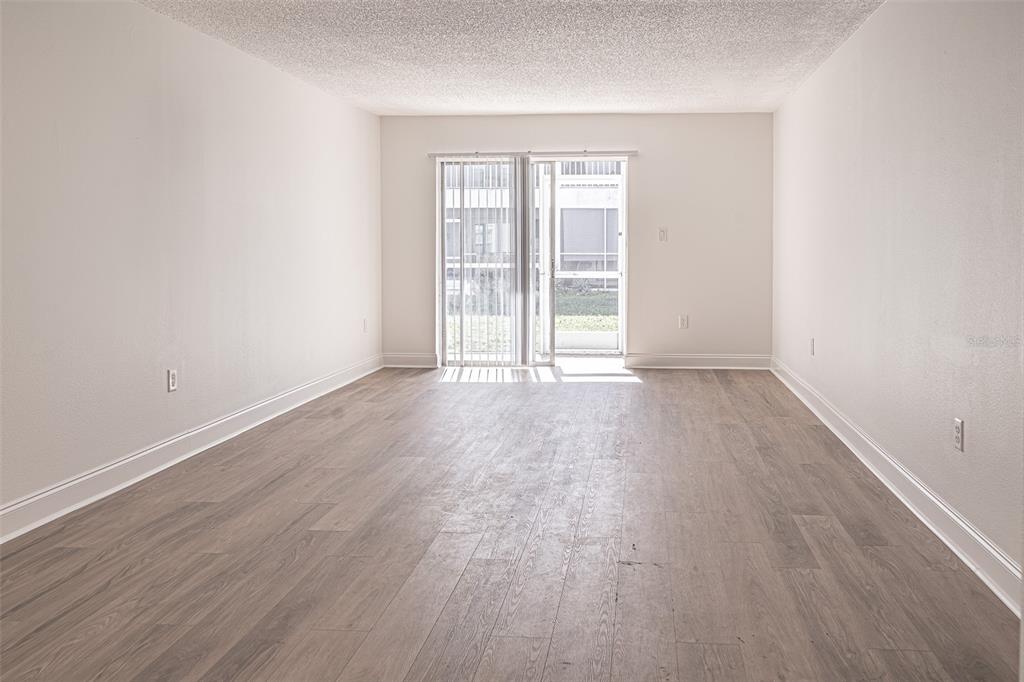 An empty room with light wood-look flooring, white walls, and a sliding glass door — 363 S MCMULLEN BOOTH ROAD UNIT 107, CLEARWATER, FL