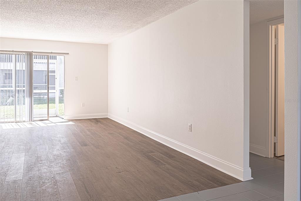 An empty room with wood-look flooring, white walls, and a sliding glass door to a patio — 363 S MCMULLEN BOOTH ROAD UNIT 107, CLEARWATER, FL