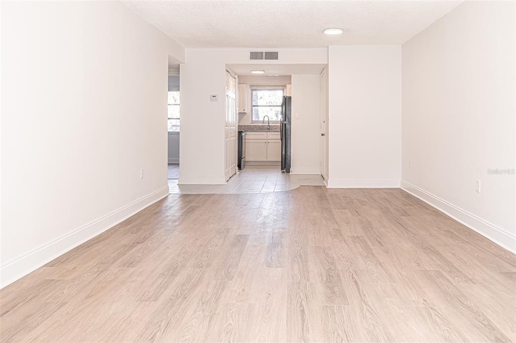 A living area with light wood-look flooring leads to a kitchen with white cabinets — 363 S MCMULLEN BOOTH ROAD UNIT 107, CLEARWATER, FL
