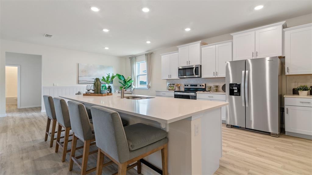 A modern kitchen features a large quartz island, white cabinetry, and stainless steel appliances — 3001 KINGSMAN TRAIL, ORMOND BEACH, FL