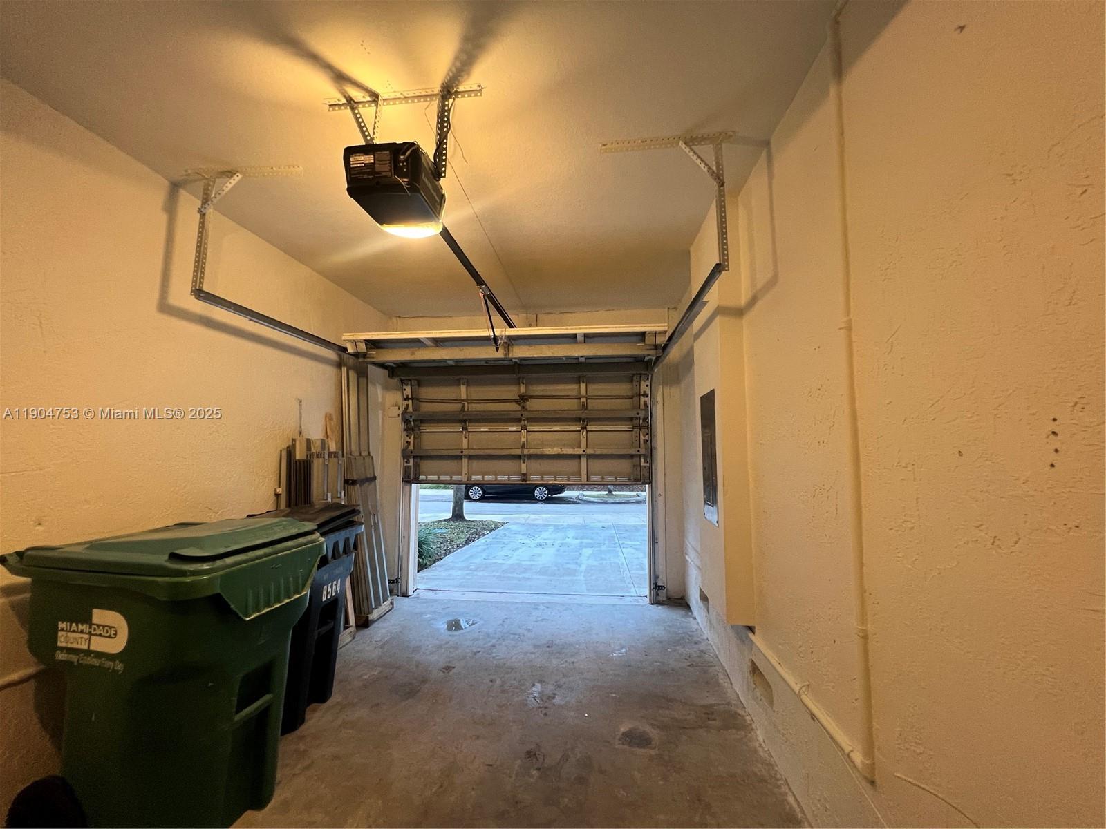 A garage interior features a concrete floor, a ceiling-mounted opener, and two large trash bins — 8564 SW 214th Way, Cutler Bay FL 33189, CUTLER BAY, FL