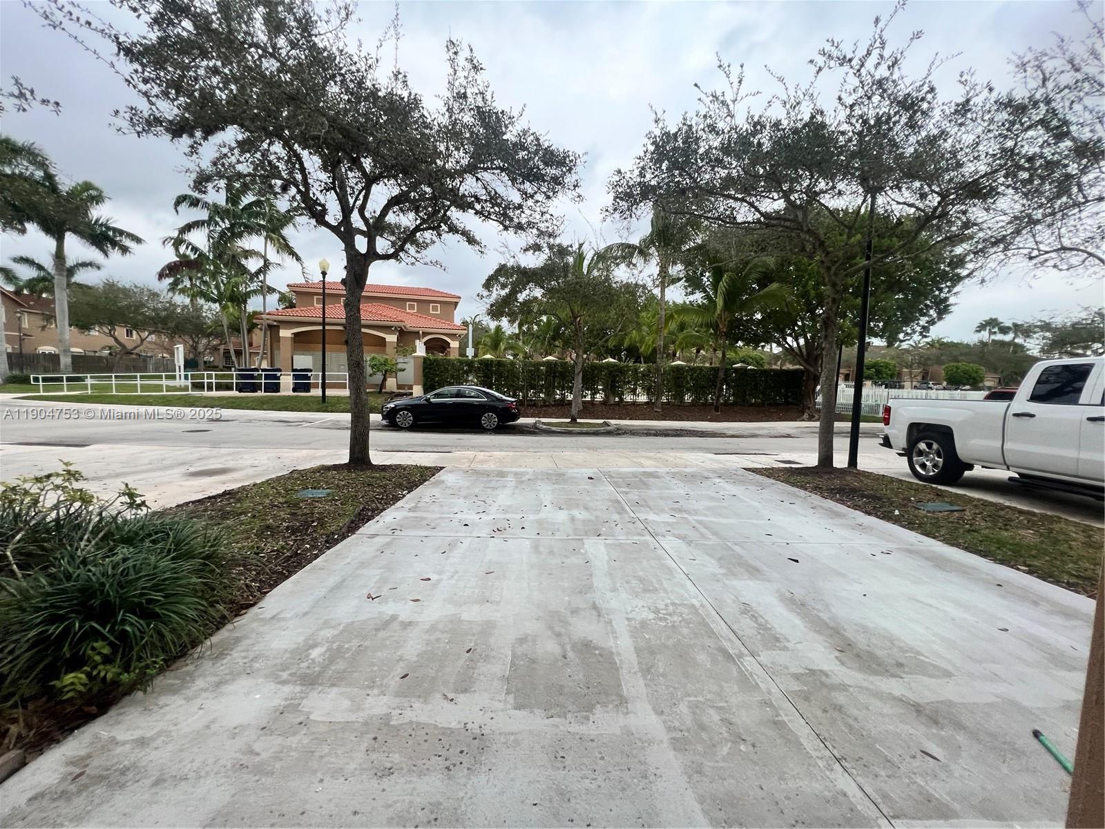 A concrete driveway leads toward a street with a parked car and a clubhouse building — 8564 SW 214th Way, Cutler Bay FL 33189, CUTLER BAY, FL