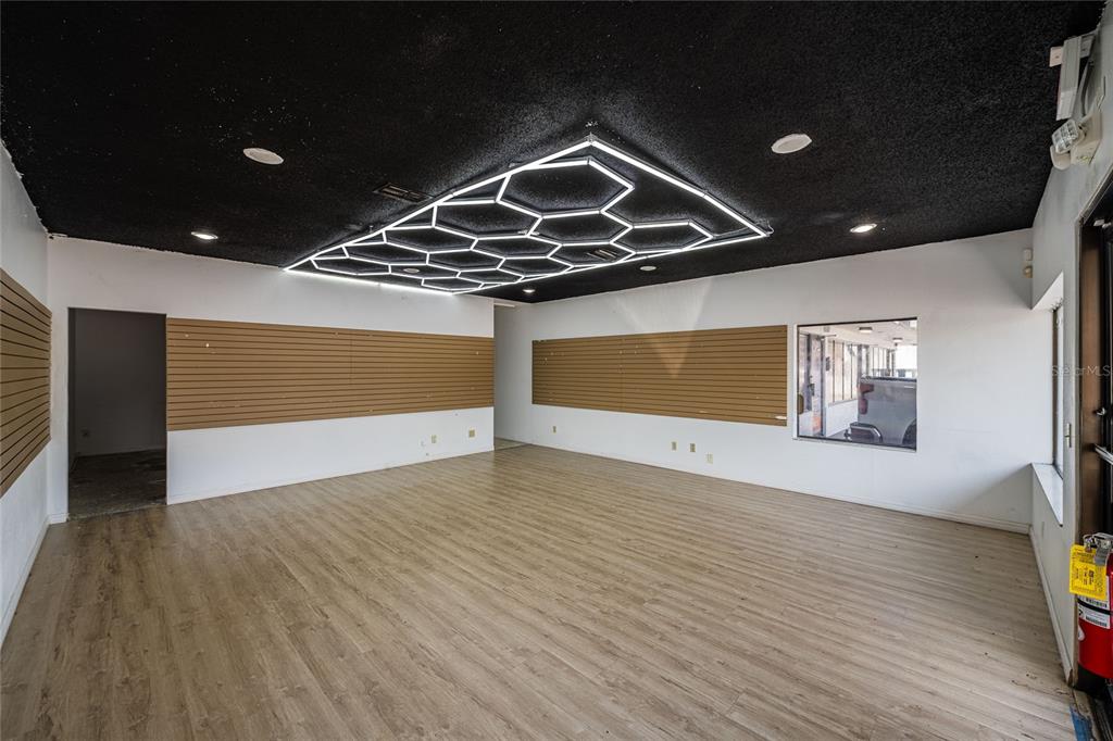 An empty commercial space features wood-look flooring, slat wall panels, and a hexagonal LED ceiling light — 211 E CENTRAL AVENUE, WINTER HAVEN, FL