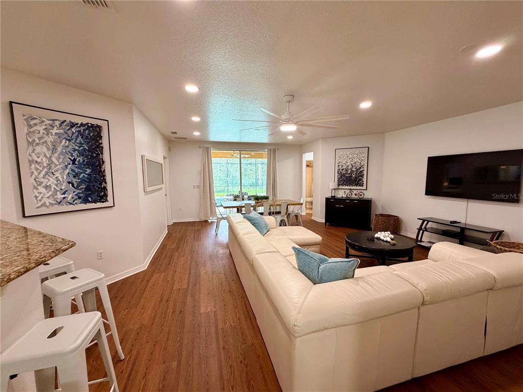 A living room features a white sectional sofa, wood-look flooring, and a large television — 9110 STROMBOLI COURT, KISSIMMEE, FL