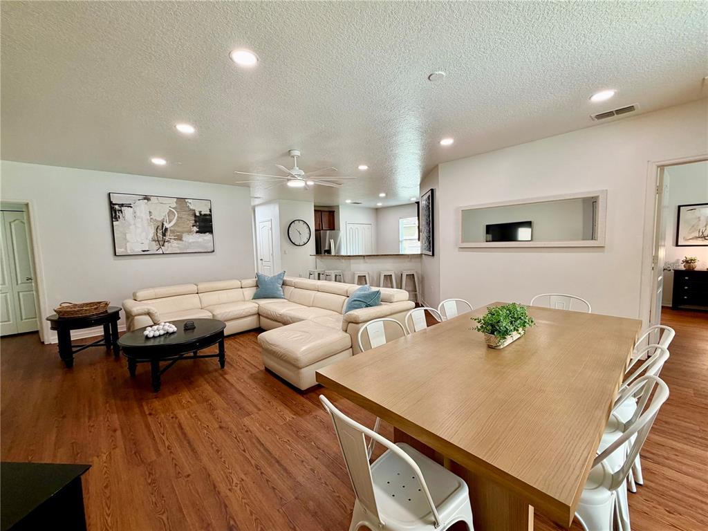 An open-concept living and dining area features wood flooring, a white sectional, and a table — 9110 STROMBOLI COURT, KISSIMMEE, FL