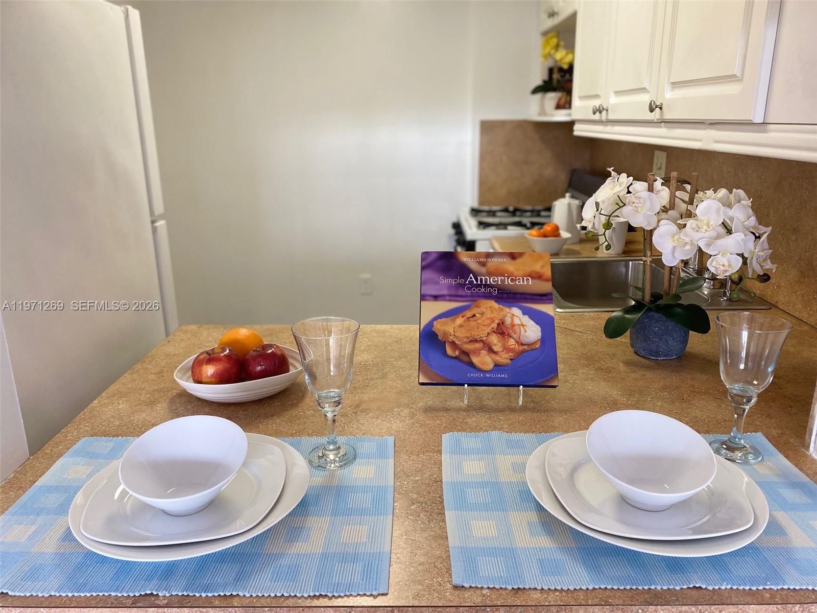 A kitchen counter is set for two with bowls, plates, glasses, and a cookbook — 13120 SW 92nd Ave # 414, Miami FL 33176, MIAMI, FL