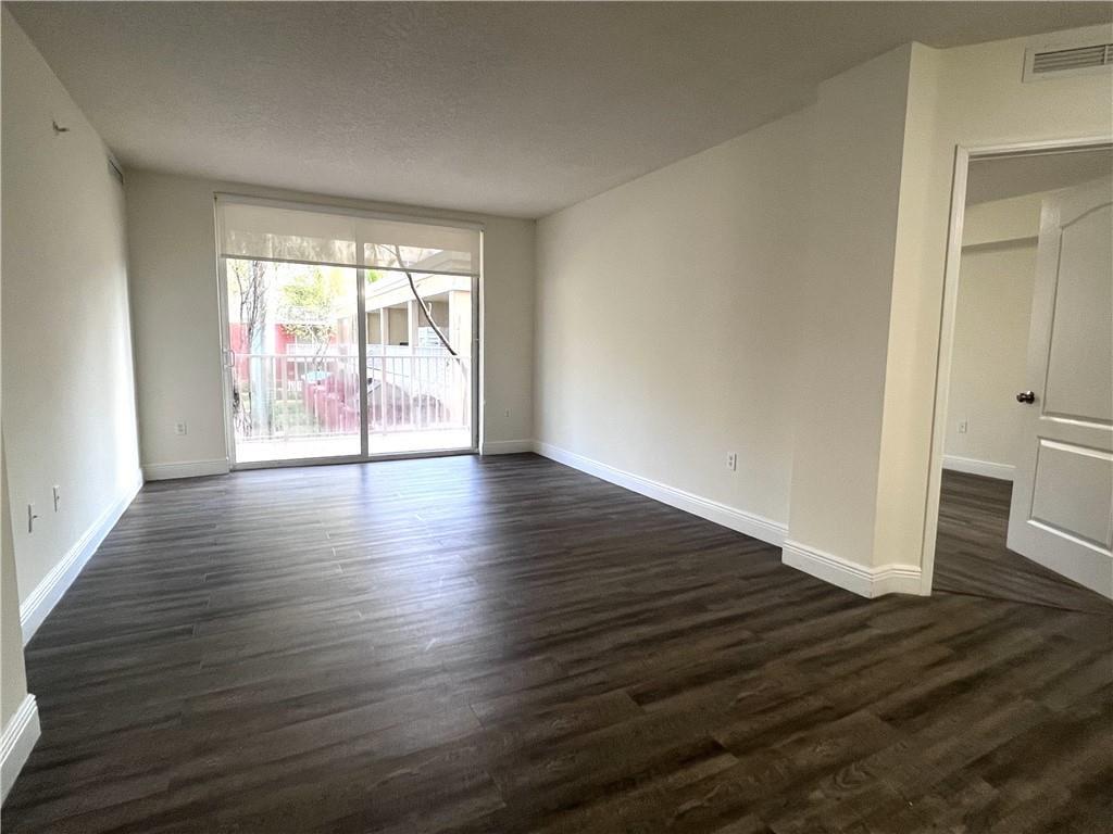 An empty living room features dark wood-look flooring, white walls, and a sliding glass door — 18335 NW 68 Avenue # 420, Hialeah FL 33015, HIALEAH, FL