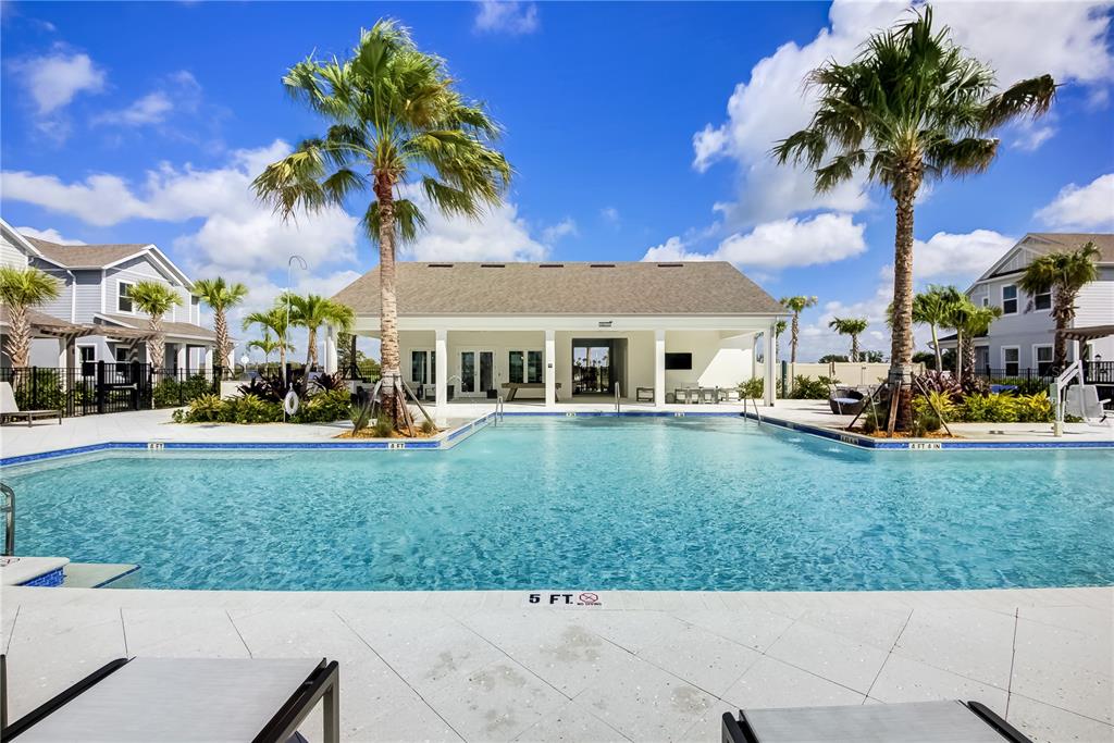 A swimming pool sits in front of a community clubhouse with palm trees under blue skies — 9131 WALCOTT LANE, LAKEWOOD RANCH, FL