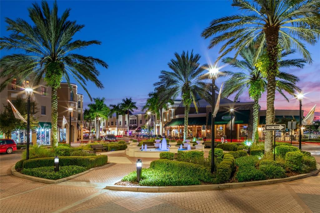 An outdoor plaza features a central fountain, manicured landscaping, and palm trees at twilight — 9131 WALCOTT LANE, LAKEWOOD RANCH, FL