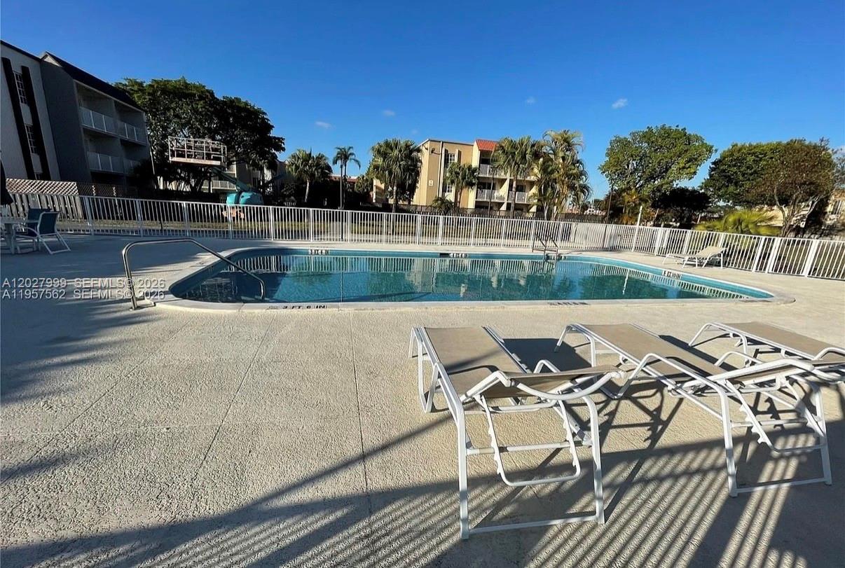 A swimming pool with lounge chairs on the deck is surrounded by a white fence — 4800 NW 79th Ave # 208, Doral FL 33166, DORAL, FL