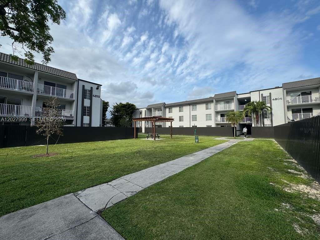 A grassy courtyard sits between two multi-story apartment buildings with a wooden pergola — 4800 NW 79th Ave # 208, Doral FL 33166, DORAL, FL