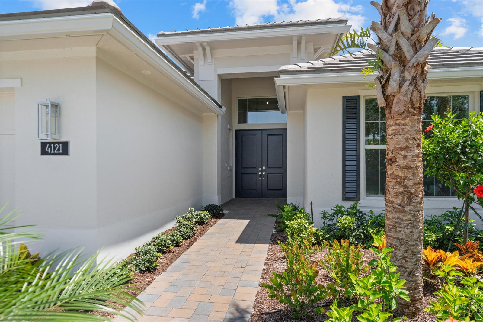 The exterior of a house features a paved walkway leading to a dark double front door — 4121 Lucaya Pointe Way, Vero Beach FL 32967, VERO BEACH, FL