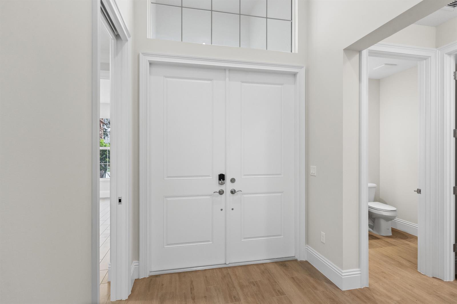 A bright entryway features double white doors, light wood flooring, and an adjacent half bathroom — 4121 Lucaya Pointe Way, Vero Beach FL 32967, VERO BEACH, FL