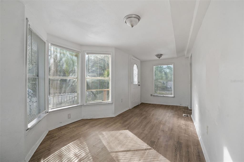An empty room features wood-look flooring, white walls, a bay window, and a glass-paneled door — 10205 BURTON STREET, NEW PORT RICHEY, FL