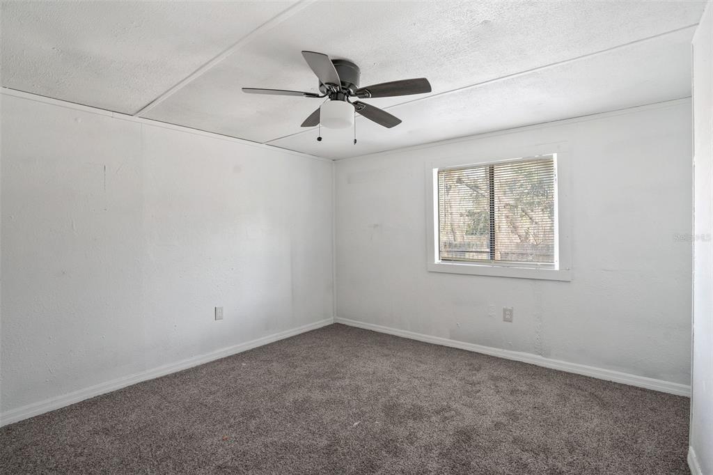 A bedroom with white walls, gray carpeting, a ceiling fan, and a single window — 10205 BURTON STREET, NEW PORT RICHEY, FL
