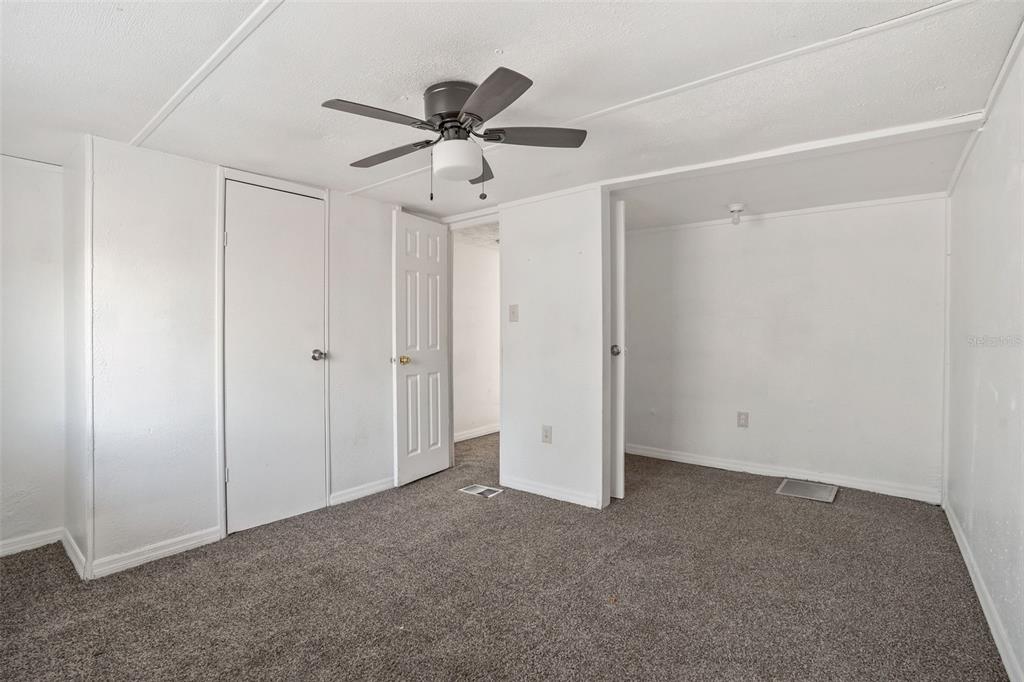 A bedroom with gray carpet, white walls, a ceiling fan, and two interior doors — 10205 BURTON STREET, NEW PORT RICHEY, FL