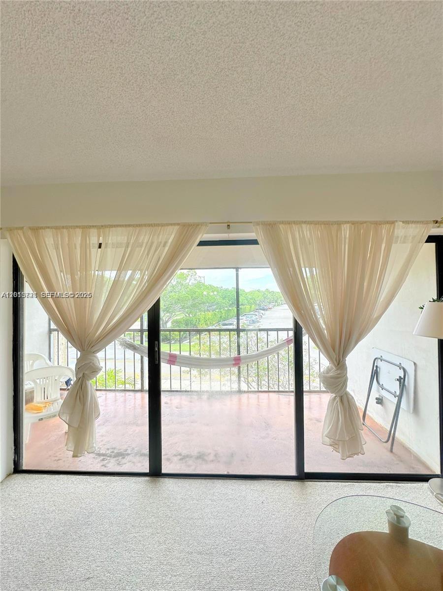 A room with beige carpet looks out through sliding glass doors onto a screened balcony — 240 Lakeview Dr # 212, Weston FL 33326, WESTON, FL