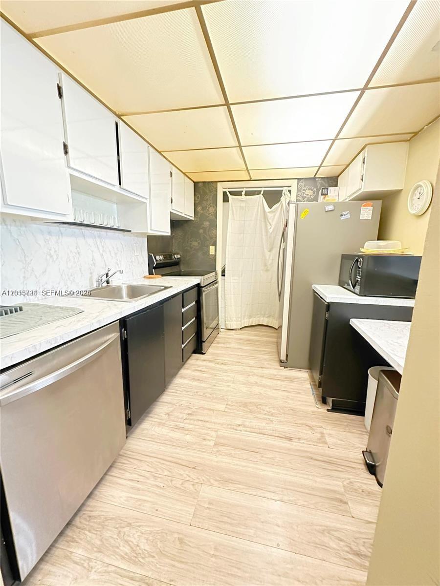 This kitchen features white upper cabinets, black lower cabinets, stainless steel appliances, and wood-look flooring — 240 Lakeview Dr # 212, Weston FL 33326, WESTON, FL