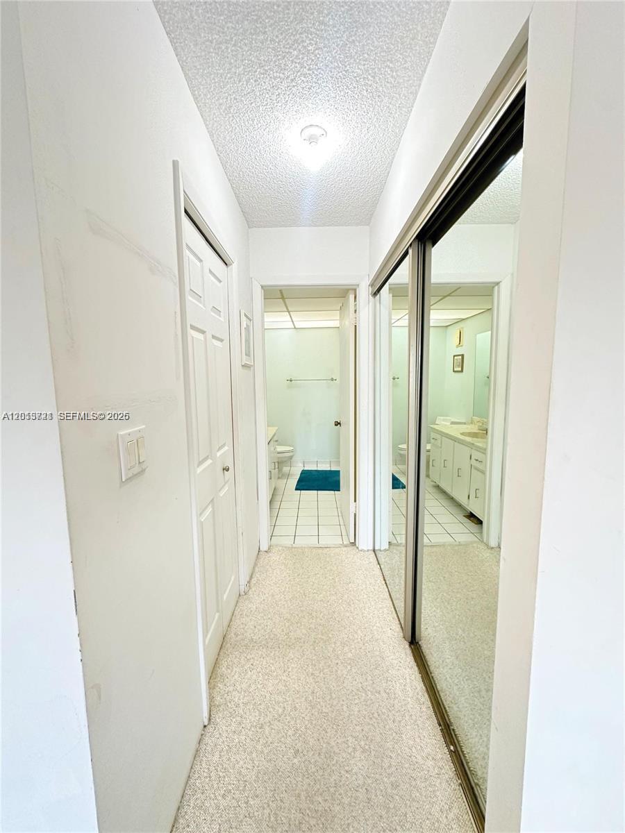 A hallway with beige carpeting leads to a bathroom with white tile flooring — 240 Lakeview Dr # 212, Weston FL 33326, WESTON, FL