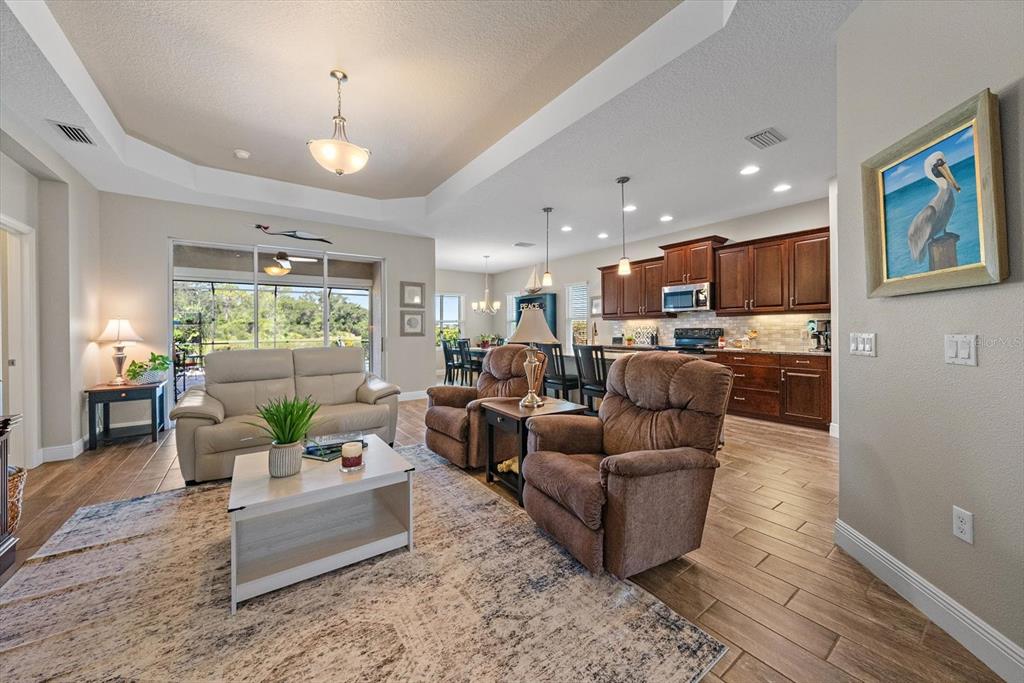 An open-concept living room features tile flooring, a tray ceiling, and an adjacent kitchen — 4716 CREEKRIDGE COURT, BRADENTON, FL