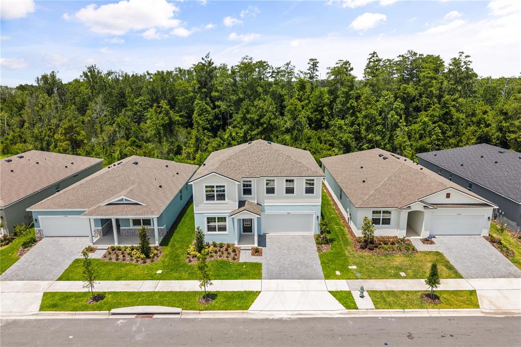 An aerial view shows three suburban houses with paved driveways and lawns bordering a forest — 13234 GENERATIONS AVENUE, ORLANDO, FL