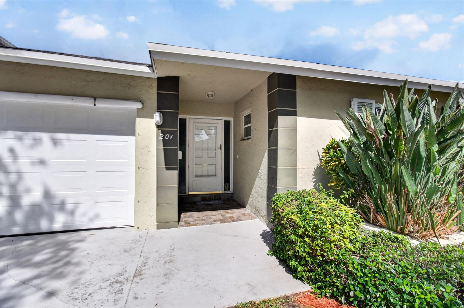 The exterior of a house features a white garage door, a front entrance, and landscaping — 201 Del Rio Boulevard, Boca Raton FL 33432, BOCA RATON, FL