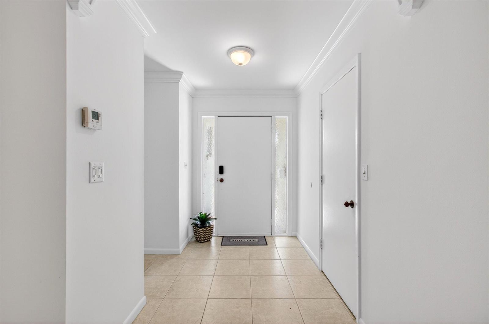 A bright entryway features white walls, tile flooring, a central light fixture, and a front door — 201 Del Rio Boulevard, Boca Raton FL 33432, BOCA RATON, FL